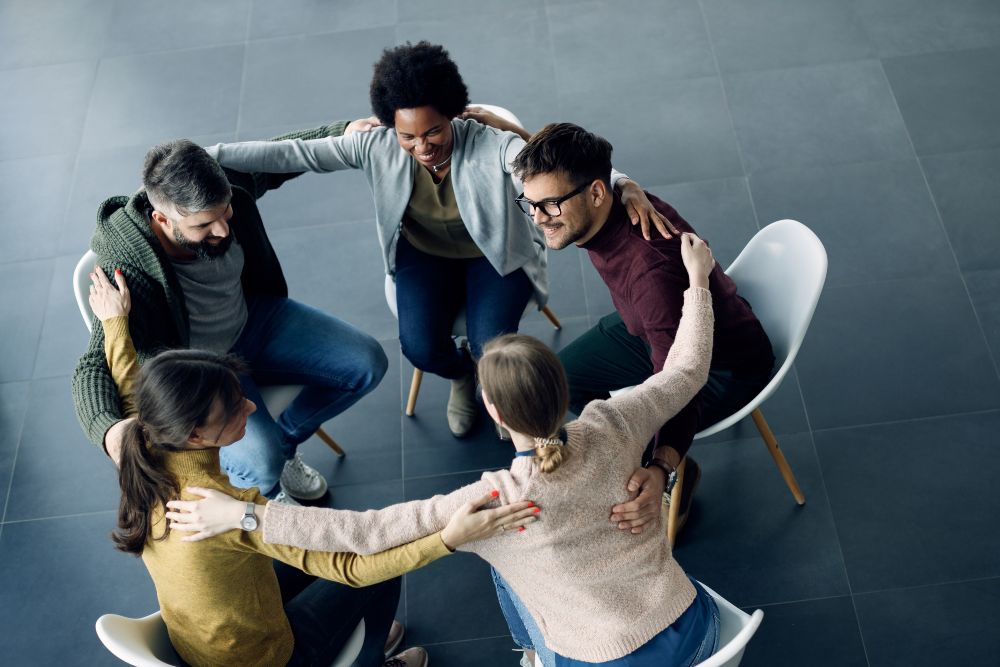 High angle view of group of supportive people sitting in a circle and embracing each other during group therapy. Copy space.